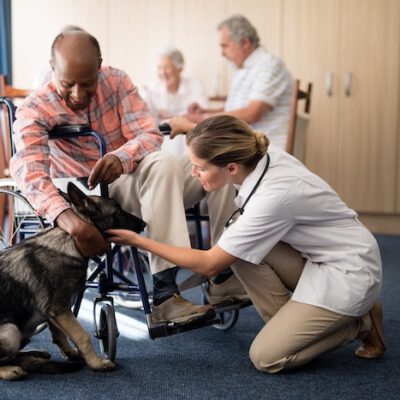 Female doctor kneeling by disabled senior man stroking puppy